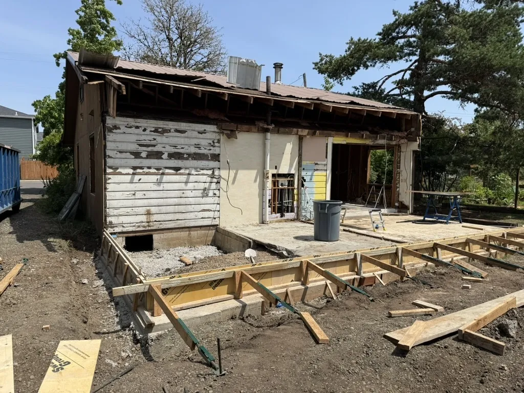 Older Philomath house mid-renovation, siding stripped and a new foundation being formed up alongside.