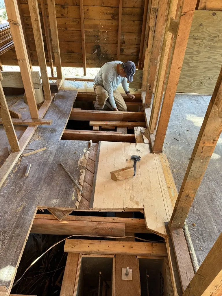 Interior framing work with floor joists cut open and tools staged, exposed wood structure.